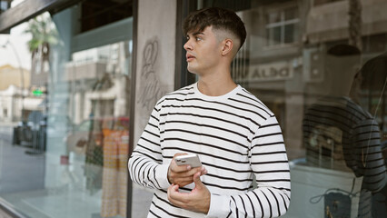 Poster - Handsome young hispanic guy takes the street, seriously immersed in texting on his cellphone under the sunny exterior, reflecting an cool urban lifestyle.