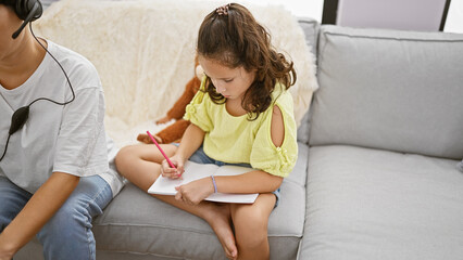 Wall Mural - Mother and daughter enjoying family love, sitting together on the living room sofa, working online and drawing in a notebook at home