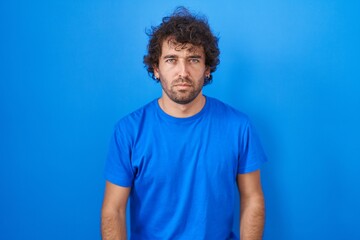 Wall Mural - Hispanic young man standing over blue background skeptic and nervous, frowning upset because of problem. negative person.