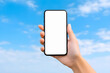 © weerasak - A hand holding a smartphone with a blank screen up to a blue sky with fluffy clouds