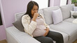 © Krakenimages.com - Young pregnant woman touching belly sitting on sofa coughing at home