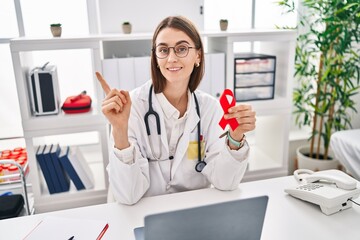 Sticker - Young caucasian doctor woman holding support red ribbon smiling happy pointing with hand and finger to the side