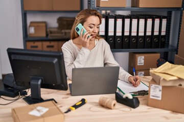 Young woman ecommerce busines worker talking on smartphone writing on document at office