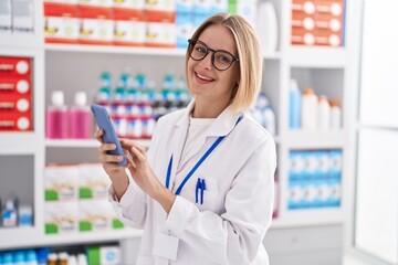 Poster - Young blonde woman pharmacist using smartphone working at pharmacy