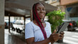 © Krakenimages.com - Confident african american woman, radiant with happiness, enjoying her touchpad at a lively coffee shop terrace, basking in the city's energetic urban vibe.