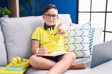 Canvas Print - Young hispanic kid doing homework sitting on the sofa pointing to you and the camera with fingers, smiling positive and cheerful