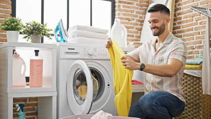 Canvas Print - Young hispanic man smiling confident washing clothes at laundry room