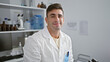 © Krakenimages.com - Confident young hispanic man, smiling happily as he embarks on his medical research, sitting at the laboratory table surrounded by high-tech medical technology and advanced chemistry equipment