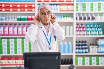 Poster - Middle age woman with tattoos working at pharmacy drugstore covering ears with fingers with annoyed expression for the noise of loud music. deaf concept.