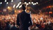 © CStock - Rear view of Motivational speaker with on stage, blurred audience,meeting of many people