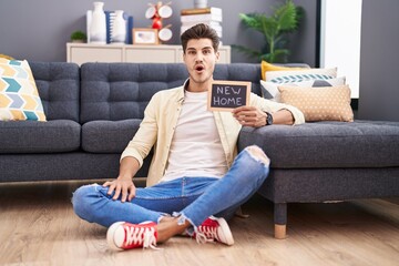 Poster - Young hispanic man holding blackboard with new home text scared and amazed with open mouth for surprise, disbelief face