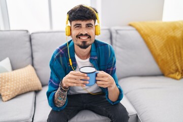 Wall Mural - Young hispanic man listening to music drinking coffee at home