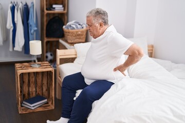 Canvas Print - Middle age grey-haired man suffering for back injury sitting on bed at bedroom