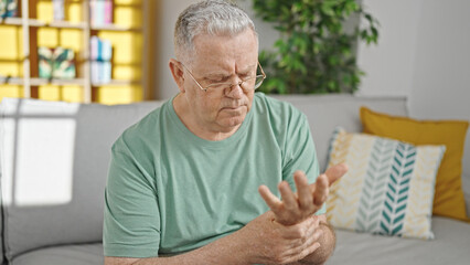 Poster - Middle age grey-haired man sitting on sofa suffering for wrist pain at home