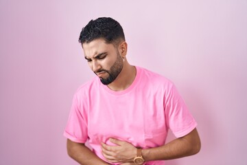 Wall Mural - Hispanic young man standing over pink background with hand on stomach because indigestion, painful illness feeling unwell. ache concept.