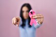 © Krakenimages.com - Hispanic woman holding pink cancer ribbon pointing with finger to the camera and to you, confident gesture looking serious