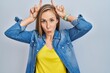 © Krakenimages.com - Young blonde woman standing over blue background doing funny gesture with finger over head as bull horns