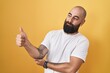 © Krakenimages.com - Young hispanic man with beard and tattoos standing over yellow background looking proud, smiling doing thumbs up gesture to the side