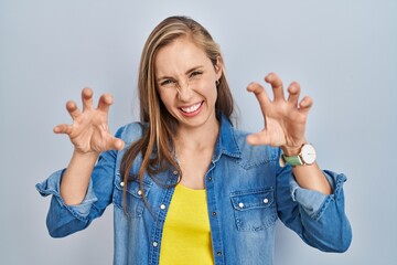 Sticker - Young blonde woman standing over blue background smiling funny doing claw gesture as cat, aggressive and sexy expression