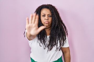 Wall Mural - Plus size hispanic woman standing over pink background doing stop sing with palm of the hand. warning expression with negative and serious gesture on the face.