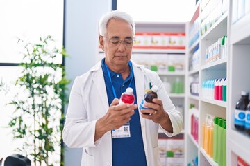 Poster - Middle age grey-haired man pharmacist smiling confident holding medication bottles at pharmacy