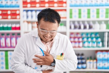 Poster - Chinese young man working at pharmacy drugstore smiling and laughing hard out loud because funny crazy joke with hands on body.