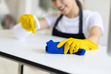 A Young Woman Wearing An Apron Is Cleaning A Table In Her Home Office Using Disinfectant And A Wipe.