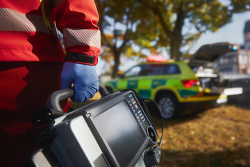 Wall Mural - Emergency medical service. Close-up of paramedic hand in blue surgical gloves while running with defibrillator monitor against ambulance car. Themes rescue, urgency and health care.