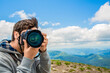 © Yevhen - Men's hands held camera closeup. Man hand holding camera looking through lens. Guy looking at photo camera, shooting photographs in the mountains. Photographer take pictures Snapshot with camera