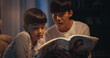 Korean Father Reading a Fairytale to His Lovely Cute Son in Bed Before Going to Sleep. Young Handsome Dad Caring for his Little boy, Reading Stories from a Book in the Evening at Home