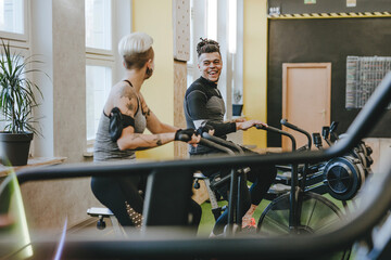 Wall Mural - Male sport trainer helping young woman riding a exercise bike during an exercise class