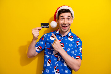 Sticker - Photo of young funny guy santa helper winter holidays begins direct fingers plastic credit card sales isolated on yellow color background