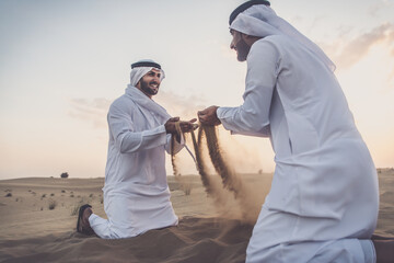 Wall Mural - Two business men wearing traditional uae white kandura spending time in the desert of Dubai