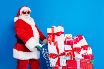 Wall Mural - Photo portrait of aged senior man push present stack trolley dressed stylish santa claus costume coat isolated on blue color background