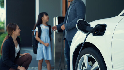 Sticker - Progressive parents with electric vehicle and home charging station. Happy family with daughter giving each other high fives before leave for school. Alternative future transportation concept of EVs