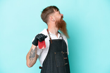 Wall Mural - Butcher man wearing an apron and serving fresh cut meat isolated on blue background laughing in lateral position