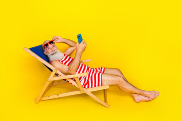 Poster - Full length photo of carefree old man lying on sunbed at turkish resort using smartphone and relaxing isolated on yellow color background