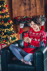 Sticker - Full length vertical photo of peaceful person sit comfy chair use smart phone x-mas shopping garland lights house indoors