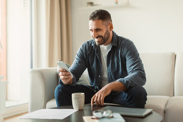 Poster - Middle aged man smiles texting via cellphone in living room