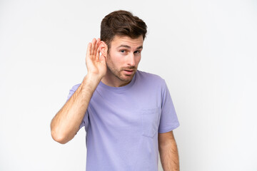 Wall Mural - Young caucasian man isolated on white background listening to something by putting hand on the ear