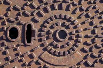 Wall Mural - Ivry-Sur-Seine, France - 09 30 2021: view of a rusty brown manhole cover under bright light.