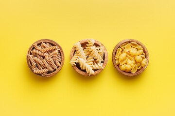 Wall Mural - Raw whole grain fusilli pasta and gnocchi pasta. Uncooked pasta on yellow background.