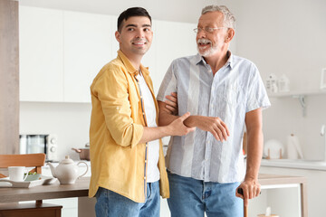 Poster - Young man helping his father with stick to walk in kitchen