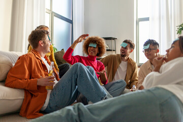 multiracial group of young friends playing charades drinking beer and having fun at home