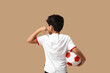 © Pixel-Shot - Little boy with soccer ball pointing at t-shirt on beige background, back view