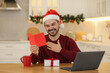 Celebrating Christmas online with exchanged by mail presents. Happy man reading greeting card during video call on laptop at home