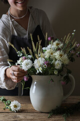 Wall Mural - Smiling woman creating beautiful flower arrangement at wooden table, closeup