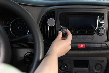 Canvas Print - Listening to radio while driving. Woman turning volume button on vehicle audio in car, closeup