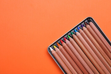 Poster - Box with many colorful pastel pencils on orange background, top view and space for text. Drawing supplies