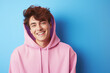 © Surachetsh - The portrait of a cute and handsome male teeager in a pink, blue hoodie standing and looking at the camera, isolated on a pink, blue background. Generative AI.